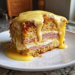 A decadent slice of eggs benedict casserole layered with ham and egg, smothered in rich hollandaise sauce.