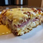 A thick slice of eggs benedict casserole layered with ham, cheese, and topped with hollandaise sauce.