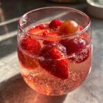 Close-up of a glass filled with fizzy pink champagne punch, strawberries, and grapes floating inside.