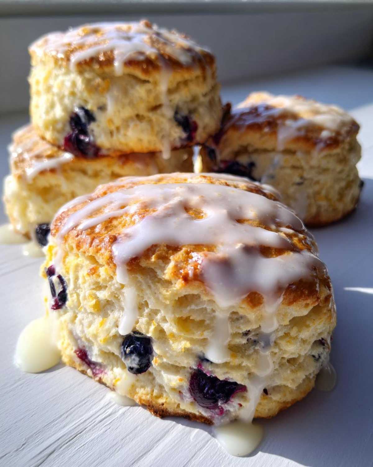 Close-up of flaky blueberry scones topped with dripping vanilla glaze, highlighting the texture.