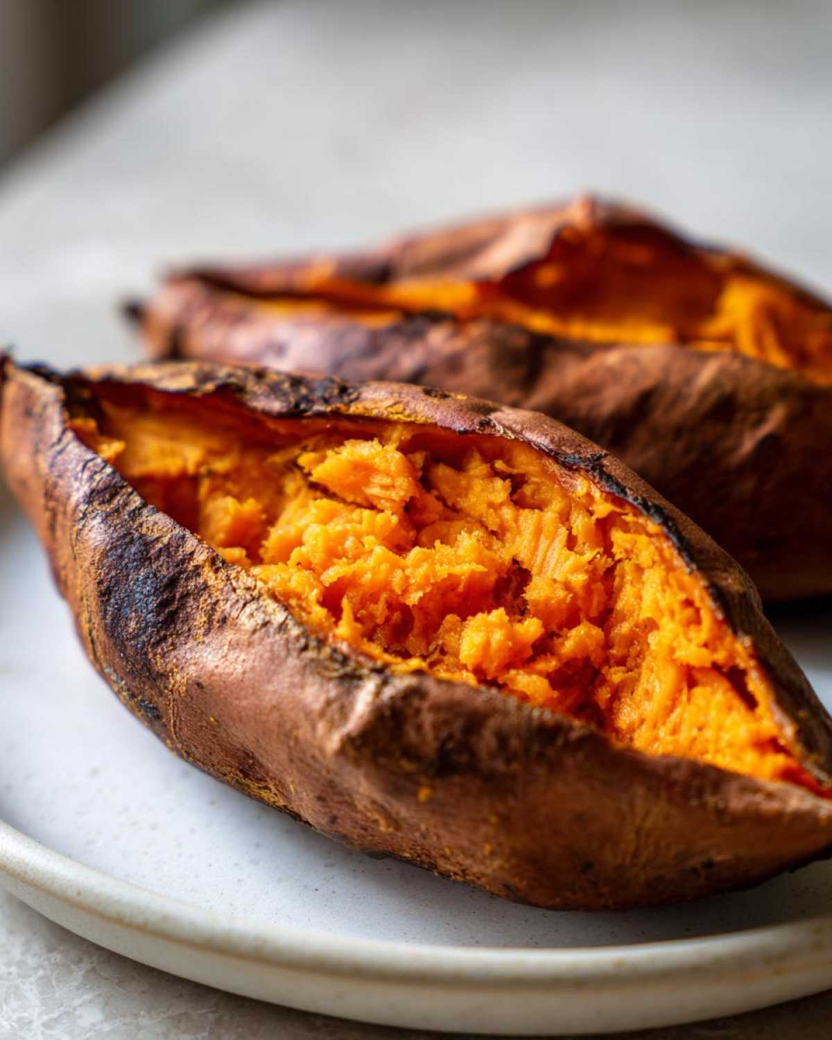 Close-up of two fluffy baked sweet potatoes, split open to show the bright orange interior.