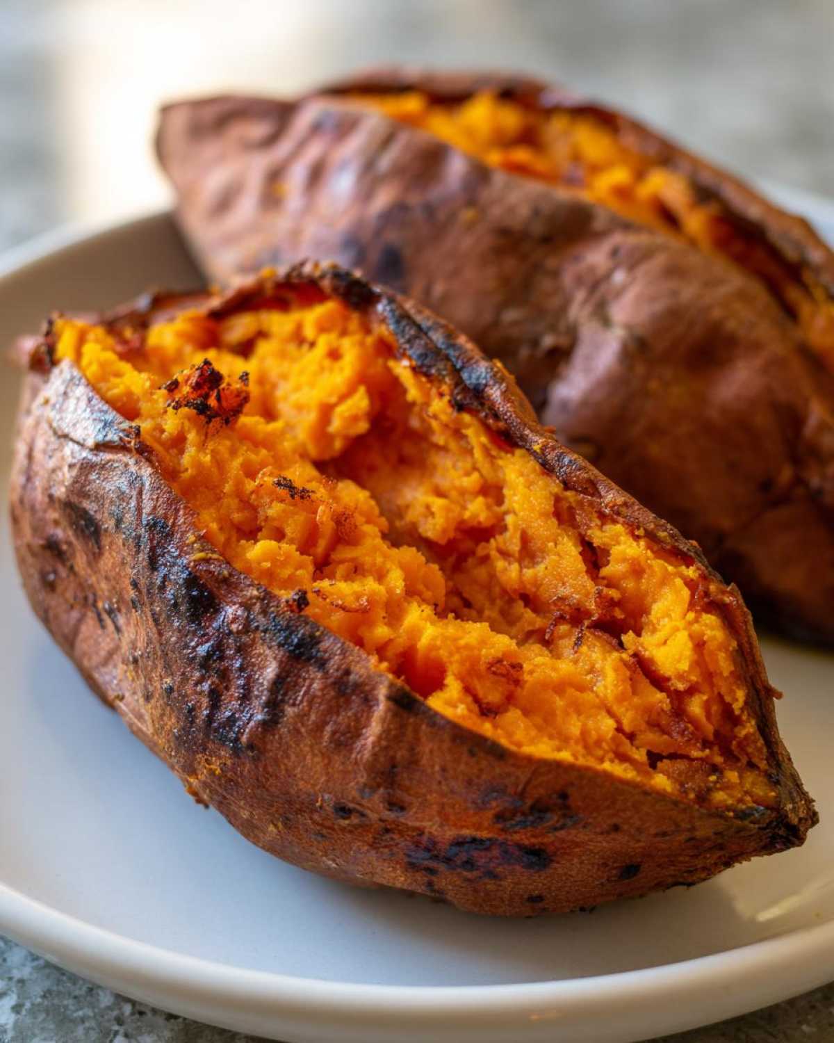 Close-up of fluffy baked sweet potatoes split open, showing bright orange flesh.