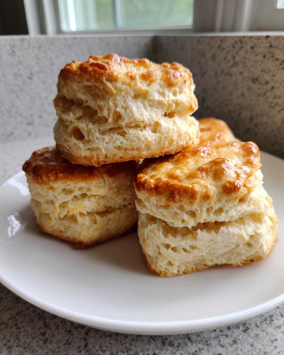 A stack of three perfectly risen, fluffy scones with golden brown tops resting on a white plate.