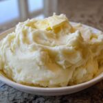 A generous serving of incredibly fluffy mashed potatoes topped with a melting pat of butter.