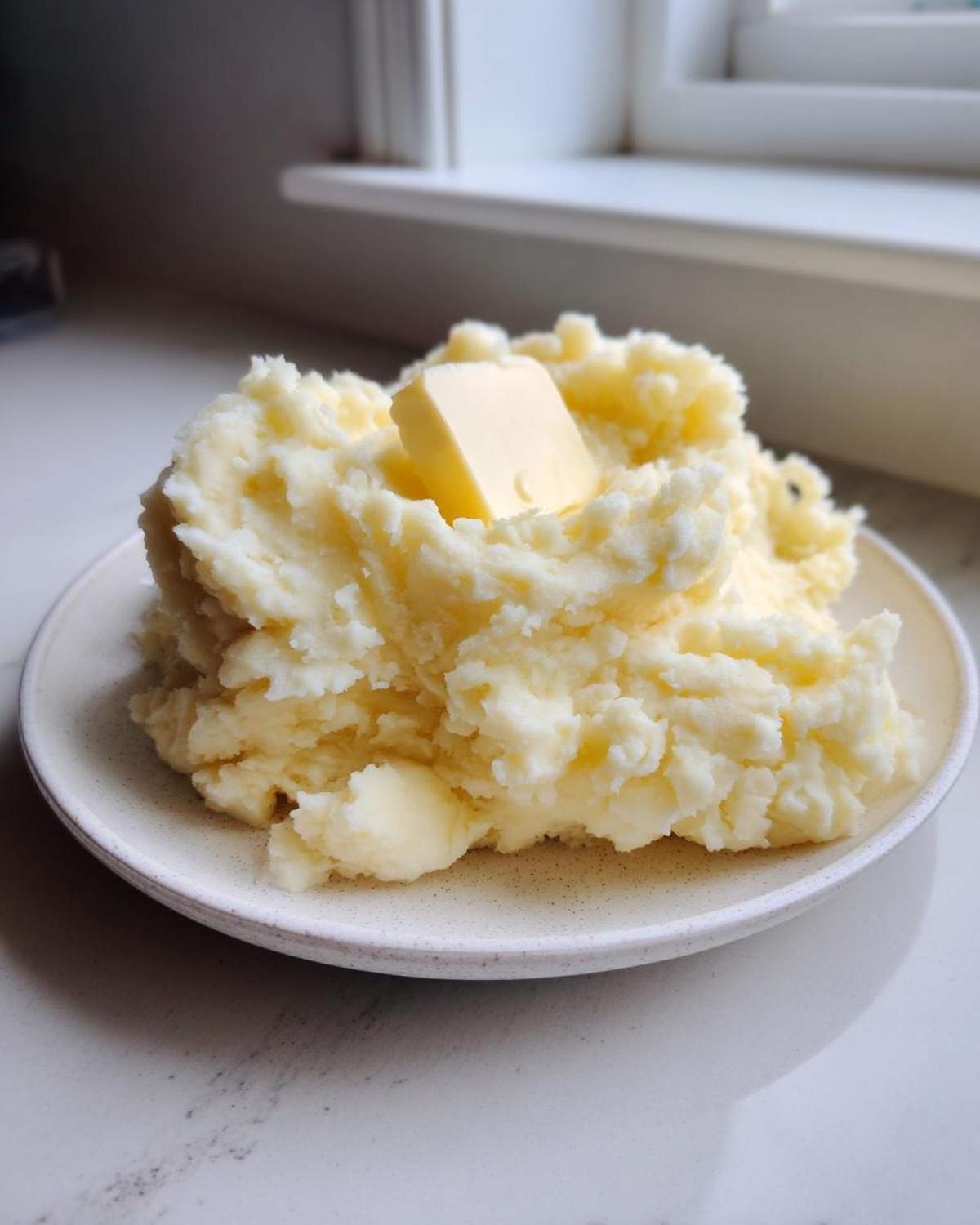A generous serving of fluffy mashed potatoes topped with a pat of melting butter.