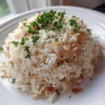 A mound of fluffy white rice pilaf topped with fresh parsley and crispy fried onions or garlic.