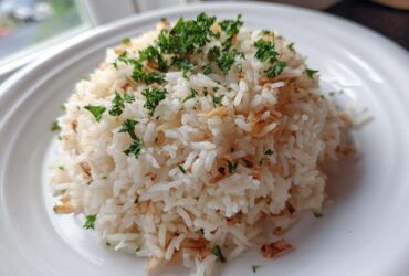 A mound of fluffy white rice pilaf topped with fresh parsley and crispy fried onions or garlic.