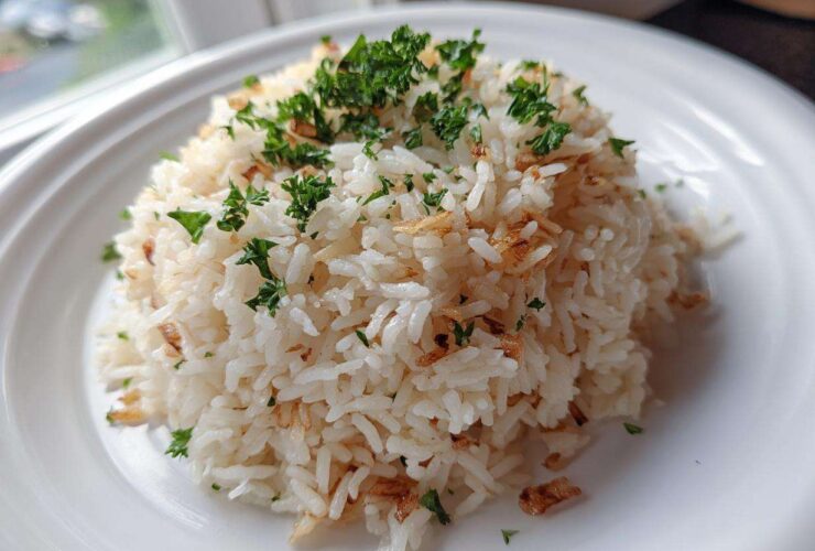 A mound of fluffy white rice pilaf topped with fresh parsley and crispy fried onions or garlic.