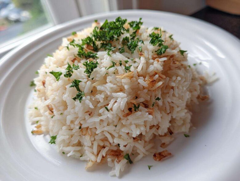 A mound of fluffy white rice pilaf topped with fresh parsley and crispy fried onions or garlic.