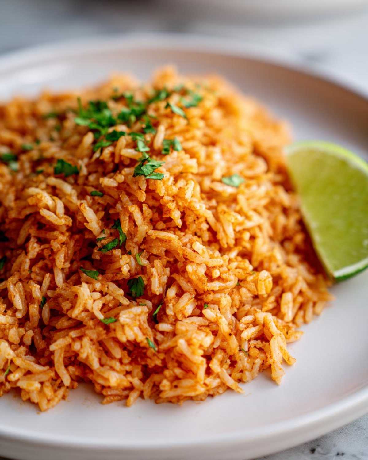 Close-up of a serving of flavorful, orange-red Spanish rice garnished with fresh cilantro and a lime wedge.