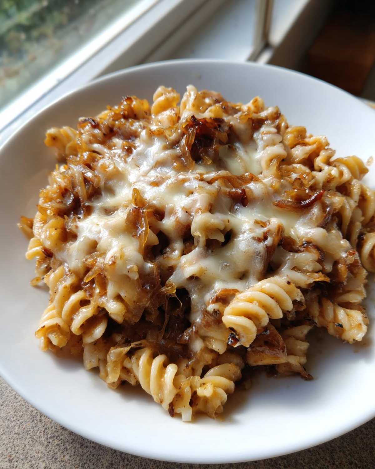 A close-up of creamy french onion pasta made with fusilli, topped with melted cheese and caramelized onions.