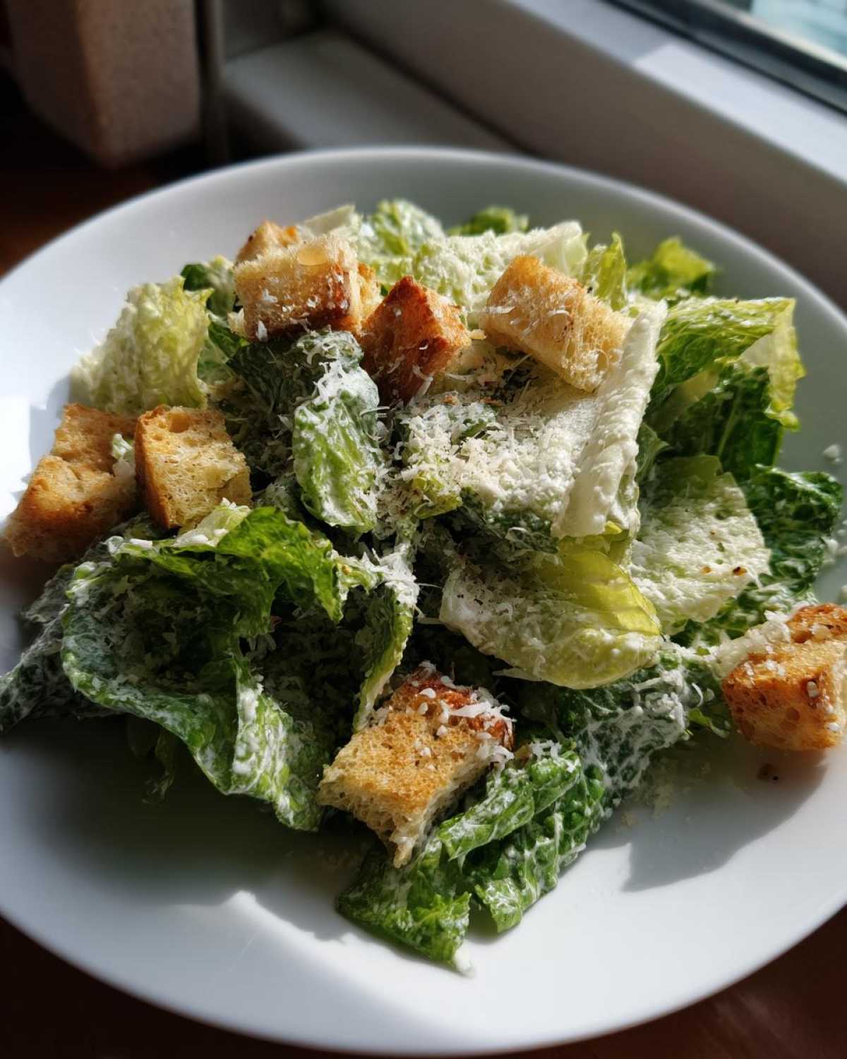A close-up of a fresh caesar salad featuring crisp romaine lettuce, creamy dressing, crunchy croutons, and grated parmesan.