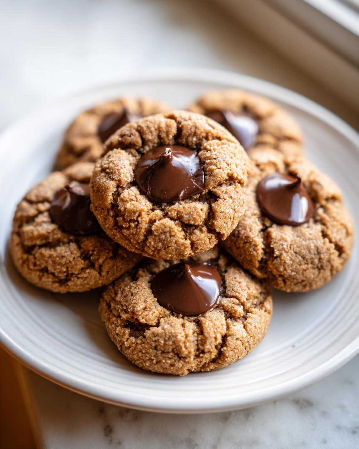 A stack of five freshly baked peanut butter blossom cookies with melted chocolate kisses on a light plate.