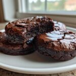 A stack of rich, fudgy chocolate brownie cookies with cracked tops, one broken open to show the gooey center.