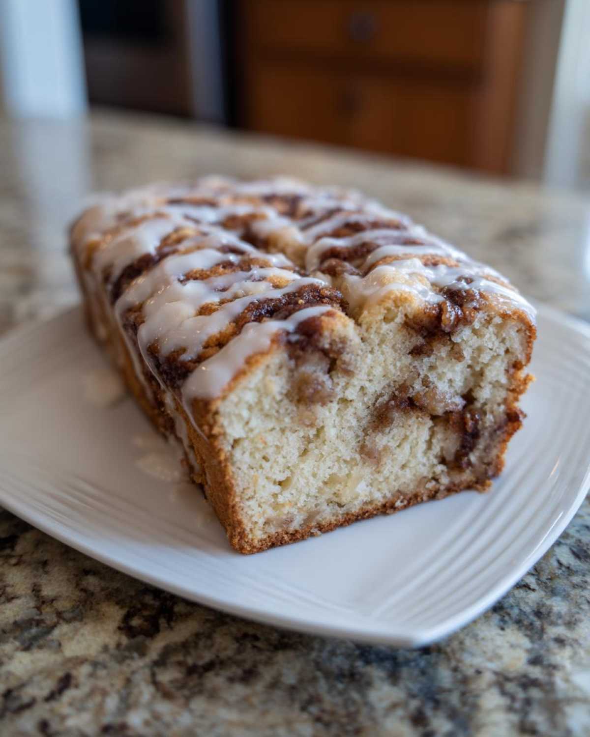 A freshly baked apple fritter bread loaf, drizzled with white icing, resting on a white plate.