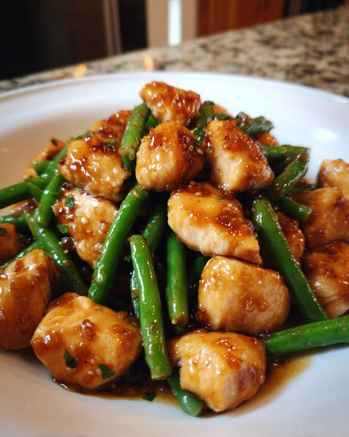 Close-up of bite-sized pieces of glazed chicken and bright green beans served on a white plate.
