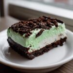 A layered slice of grasshopper pie featuring a dark chocolate crust, white filling, and mint green layer topped with chocolate crumbs.