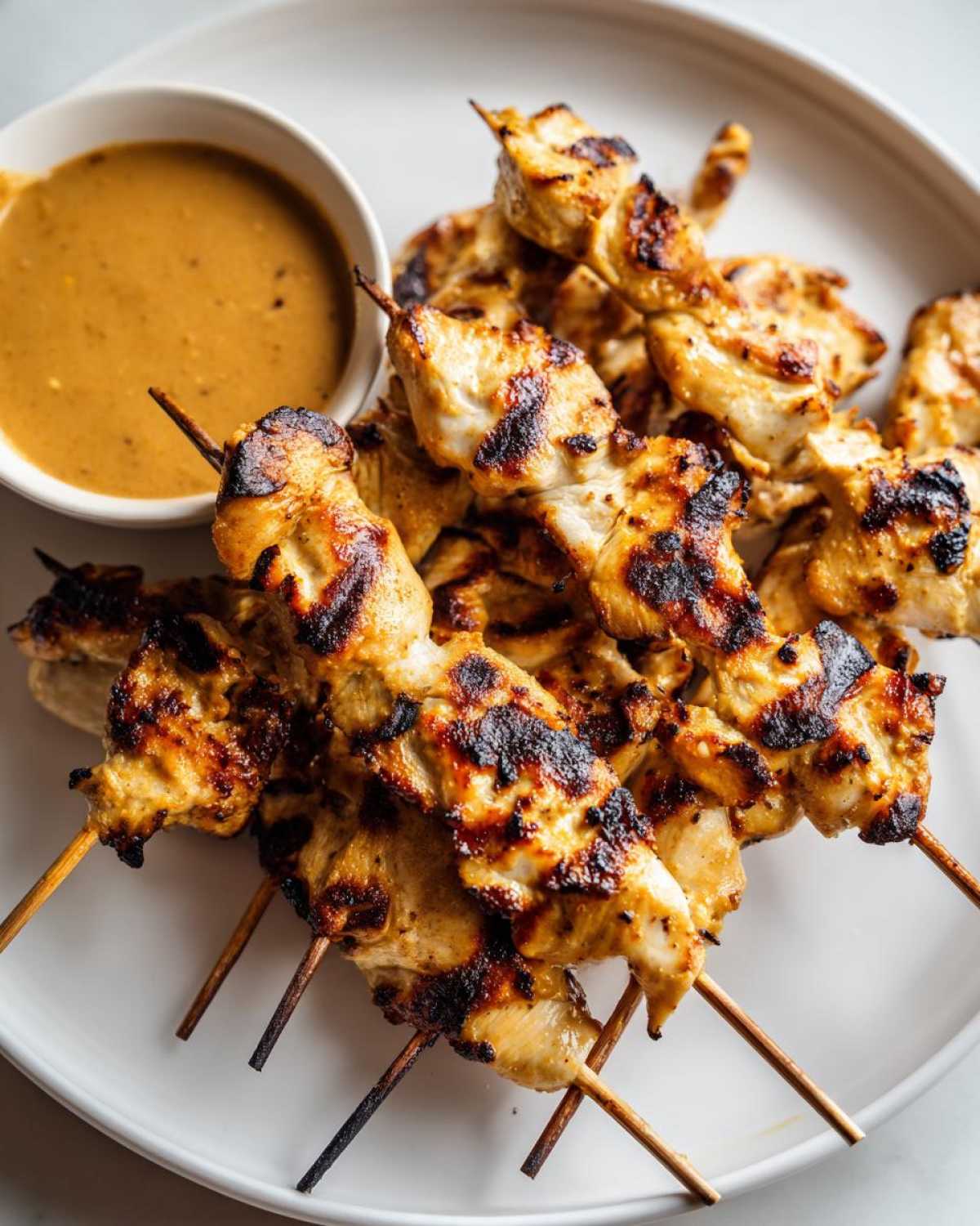 Close-up of grilled chicken satay skewers served next to a small bowl of peanut sauce.