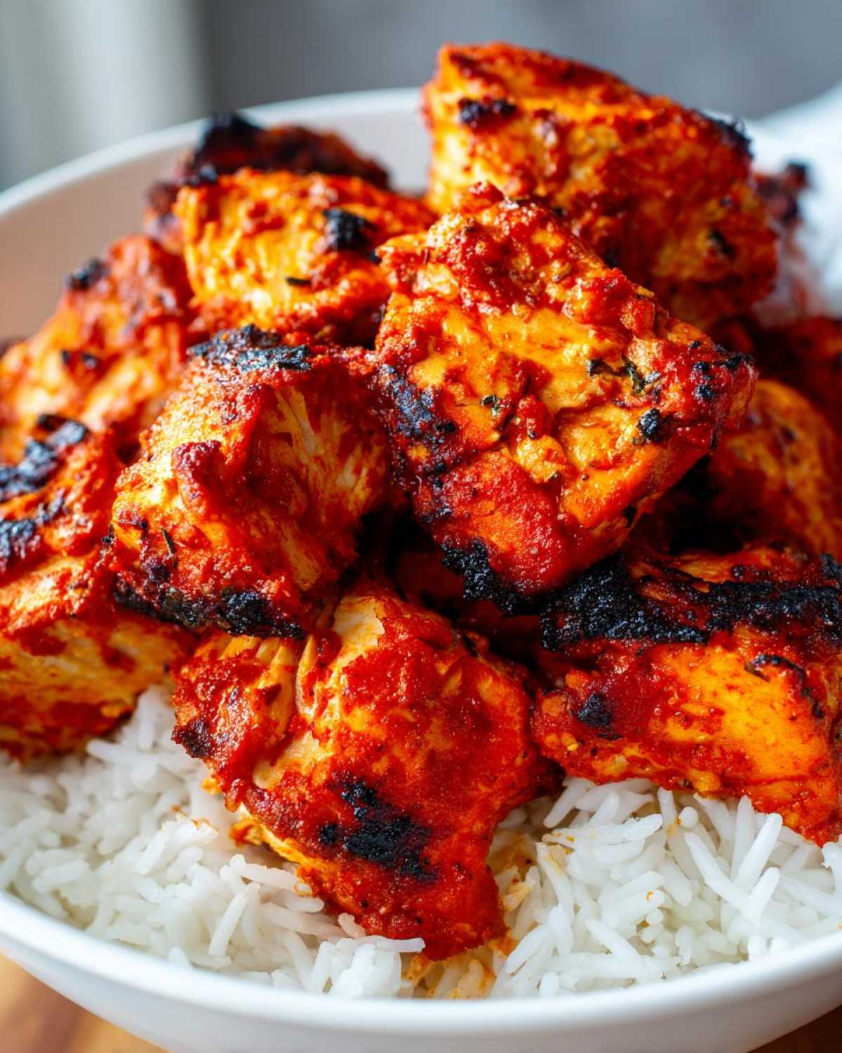 Close-up of vibrant, charred harissa chicken pieces piled high on a bed of fluffy white rice in a white bowl.