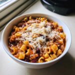 Close-up of a white bowl filled with hearty pasta fagioli topped with grated Parmesan cheese.