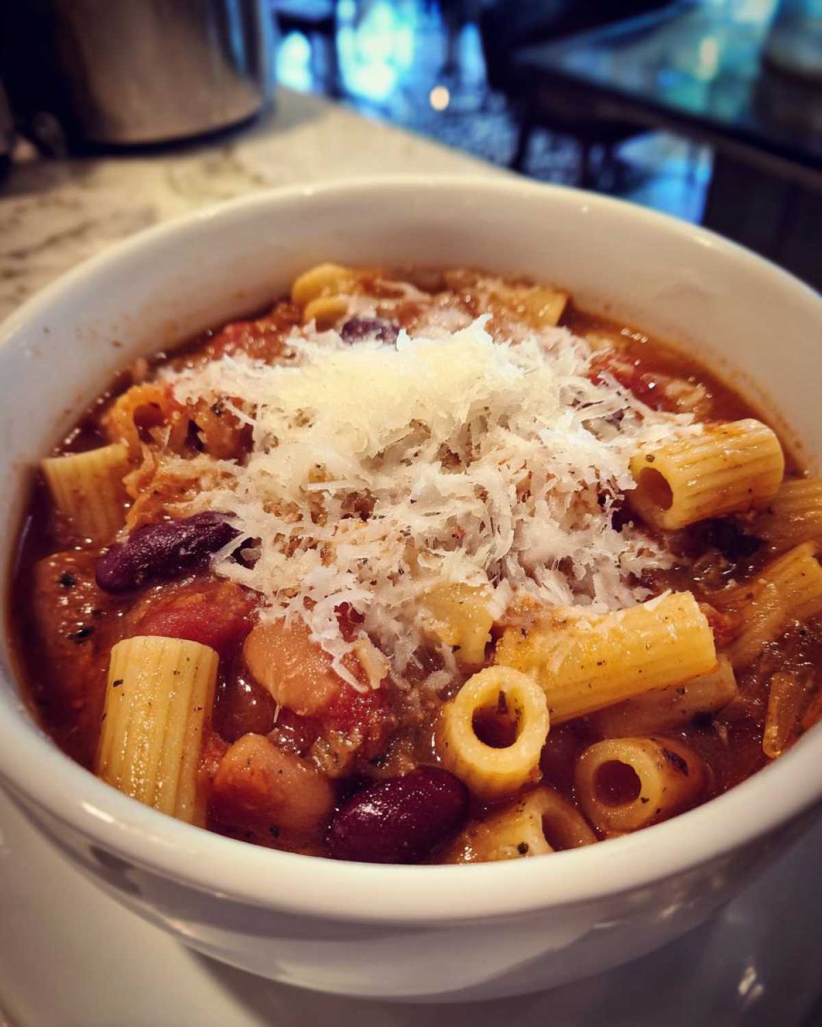 Close-up of a white bowl filled with hearty pasta fagioli, topped generously with grated Parmesan cheese.