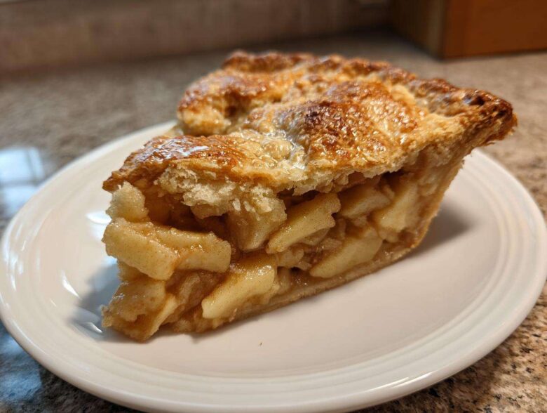 Close-up of a thick slice of homemade apple pie showing flaky crust and cinnamon-spiced apple filling.
