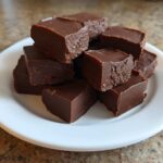 A stack of rich, dark chocolate fudge squares piled high on a small white plate.