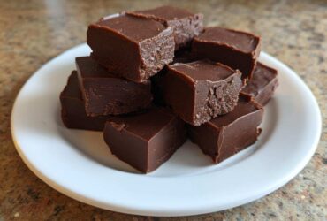 A stack of rich, dark chocolate fudge squares piled high on a small white plate.