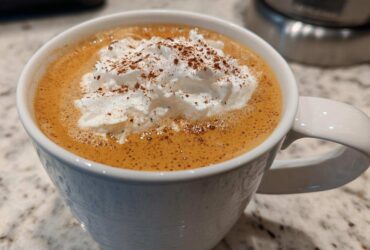 Close-up of a homemade pumpkin spice latte in a white mug, topped with whipped cream and cinnamon.