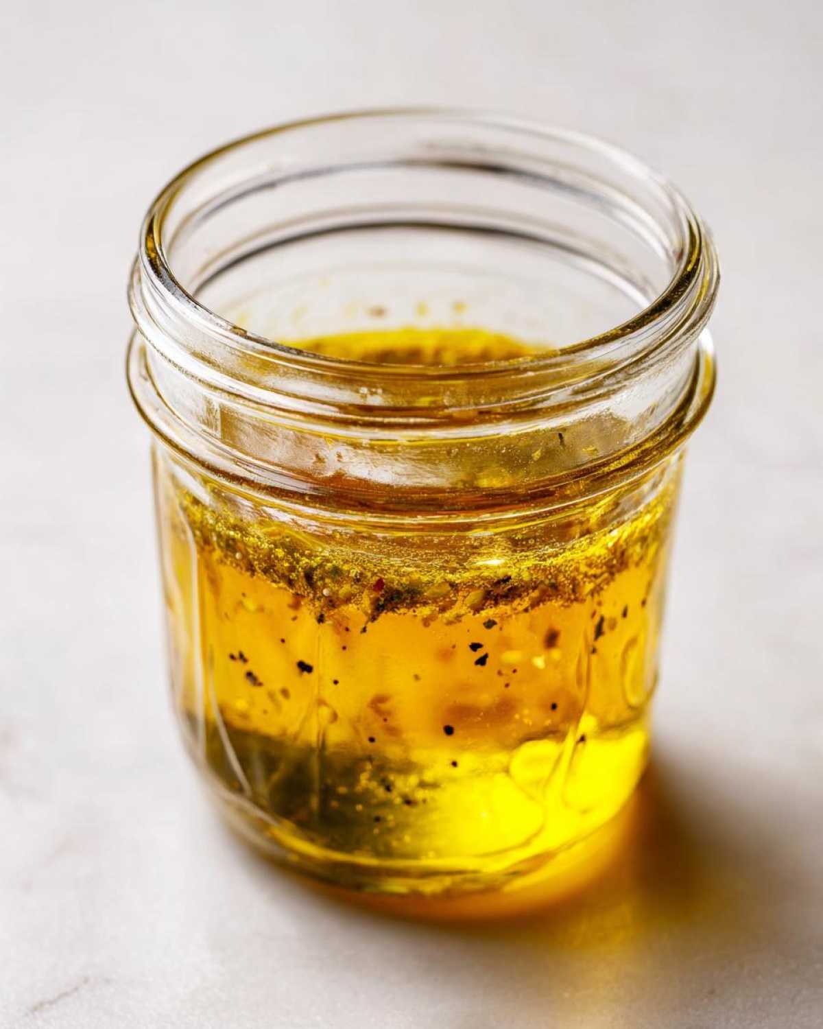 Close-up of homemade salad dressing, showing separated oil and spices, in a small glass jar.