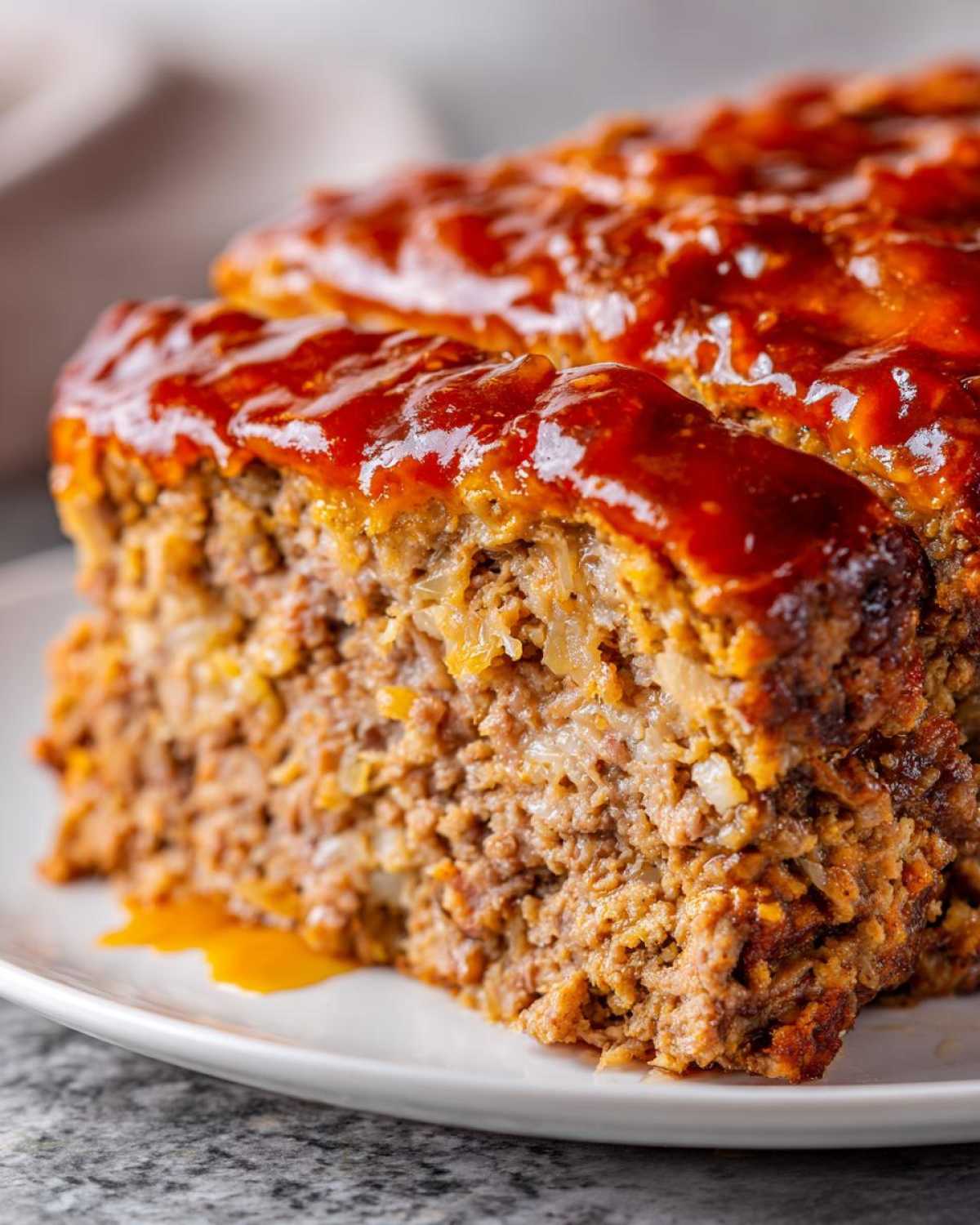 Close-up of a thick slice of juicy meatloaf topped with a shiny, thick glaze.