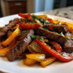 Close-up of juicy steak fajitas featuring sliced steak, red and yellow peppers, and onions, garnished with herbs.