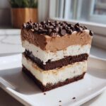 A tall slice of layered brownie refrigerator cake featuring chocolate brownie, white cream, and chocolate mousse topped with mini chips.