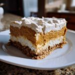 A square slice of layered pumpkin crunch dessert showing a crust, white layer, orange pumpkin layer, and whipped topping.