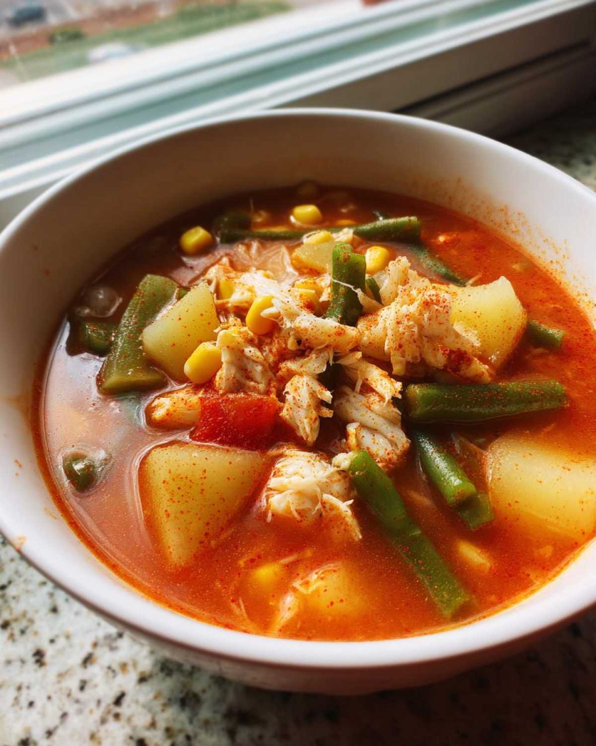 Close-up of a white bowl filled with vibrant Maryland crab soup, featuring chunks of crab meat, potatoes, green beans, and corn.