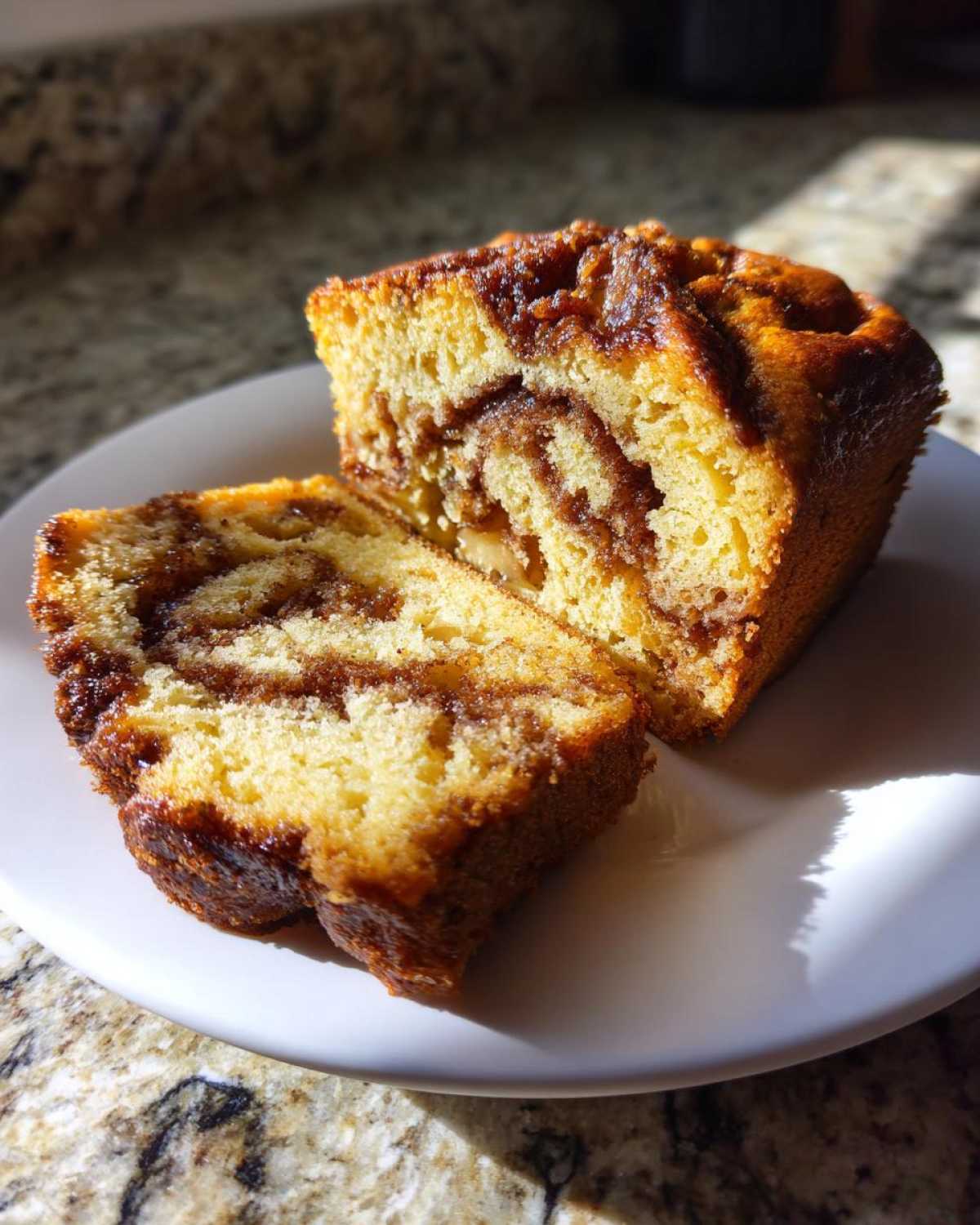 Two slices of moist apple bread showing a rich cinnamon swirl filling, served on a white plate.