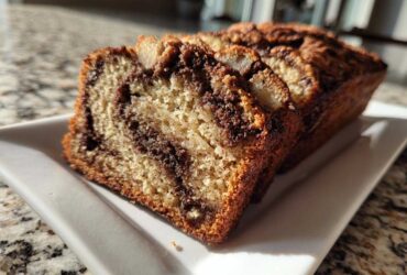 Close-up of several moist slices of cinnamon swirl apple bread served on a white rectangular plate.