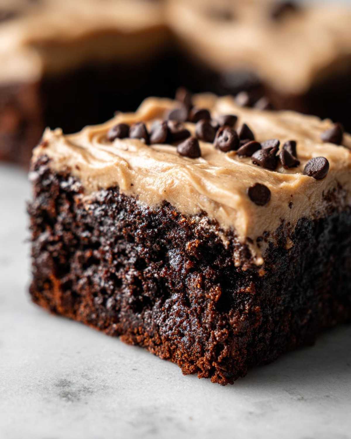 Close-up of a rich, dark chocolate banana bread brownies square topped with peanut butter frosting and mini chocolate chips.