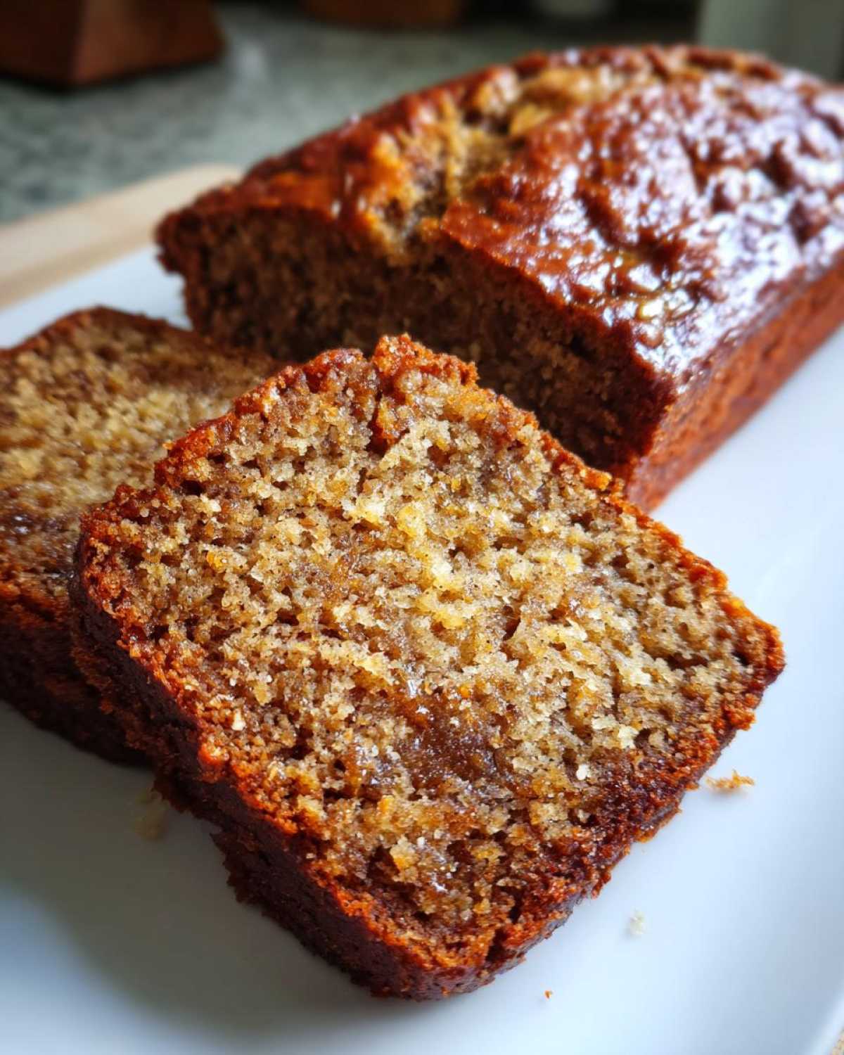 Close-up of two moist slices of banana bread next to the main loaf, showing rich texture.