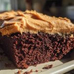 Close-up of a rich, dark brown slice of gingerbread cake topped with thick, textured peanut butter frosting.
