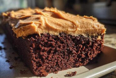 Close-up of a rich, dark brown slice of gingerbread cake topped with thick, textured peanut butter frosting.