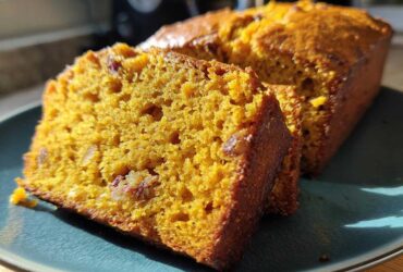 Close-up of two moist slices of bright orange pumpkin bread with visible nuts on a teal plate.