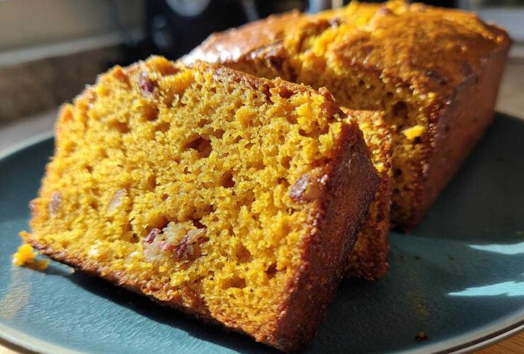 Close-up of two moist slices of bright orange pumpkin bread with visible nuts on a teal plate.