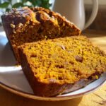 Close-up of two slices of moist, orange-colored pumpkin bread topped with chopped nuts on a plate.