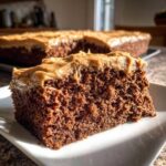 Close-up of a moist slice of dark gingerbread cake topped with thick, creamy brown frosting.