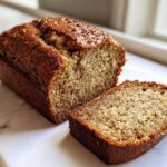 A freshly baked zucchini banana bread loaf, partially sliced, showing the moist interior texture.