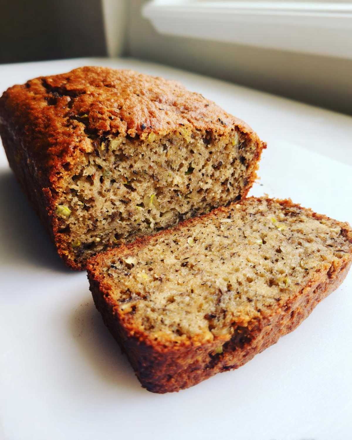 A close-up of a freshly baked zucchini banana bread loaf with one thick slice cut off, showing the moist interior.