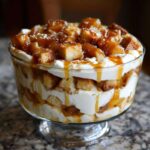 Layers of cake, cream, and spiced apples topped with caramel sauce in a glass caramel apple trifle.
