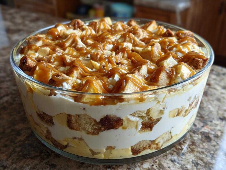 Close-up of a layered no-bake caramel apple trifle featuring cake cubes, cream, and a generous caramel drizzle on top.