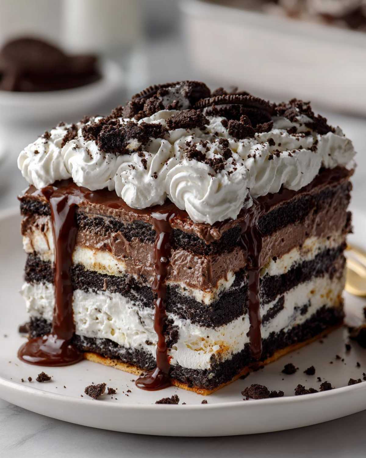 A tall, layered slice of no-bake ice cream cake featuring dark chocolate layers, white cream, chocolate mousse, and topped with whipped cream and fudge.